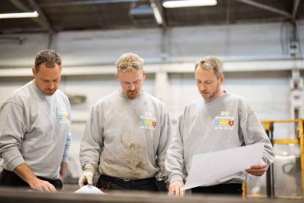 Tre medarbejdere i gråt arbejdstøj diskuterer en opgave